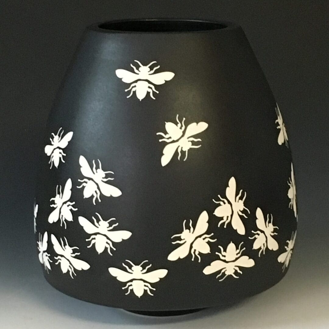 A black vase with white bees on it.