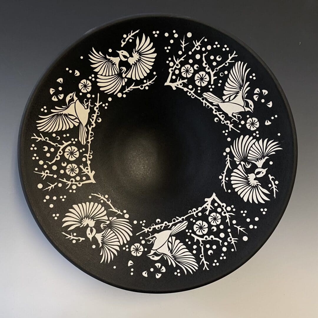 A black bowl with white birds and flowers on it.